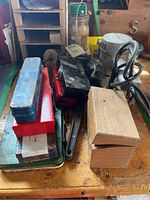 Overview of stacked tool boxes, pipe wrench handle, wooden blocks, power sander and cord visible on workbench.