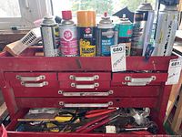Red metal toolbox filled with various spray cans, tools, and hardware items.