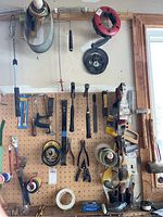Pegboard wall displaying assorted hand tools such as hammers, pliers, hand saw, and tape rolls.