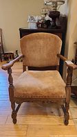 Front view of vintage armchair showing carved wooden arms, legs and rose velour upholstery on seat and back