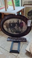 Oval vintage family portrait in dark wood frame with scratches and domed glass, showing eight individuals in black and white.