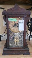 Front view of vintage Ansonia clock showcasing wooden gingerbread design, clock face with Roman numerals, and decorative glass door.