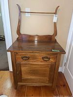 Front view of the vintage wooden washstand showing drawer, cabinet door, curved wooden back support, and caster wheels.