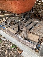 Close-up of the front wheel and metal frame showing rust and wear on the steel bucket wheelbarrow.