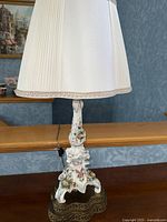 Side view of a tall porcelain lamp with white pleated shade, floral decals and ornate base