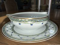 White porcelain gravy boat sitting on matching saucer with blue floral vine motif and gold trim