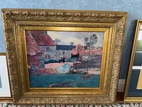 Framed canvas transfer art showing a village scene with buildings, a well, a person, and a dog near water.