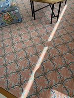 Close-up image showing wool rug pattern with pale pink/raspberry color and blue, white vine pattern.