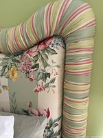 Detail of scalloped top corner of upholstered headboard showing striped green, pink and yellow fabric.