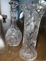 Crystal wine decanter and tall vase showing intricate floral and textured cut patterns.