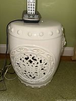 Full view of the white ceramic garden stool with a cordless phone on top, showing the overall shape and surface details.