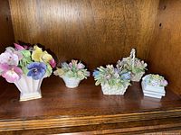 All five porcelain floral baskets and vase displayed on wooden shelf