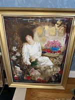 Full view of a framed mixed-media painting depicting a seated woman in white holding greenery, in an ornate gold frame