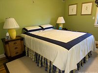 Full view of bed with coverlet, shams, bedskirt, side tables, lamps and botanical prints