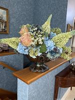 Full view of the floral centerpiece showing artificial pastel floral arrangement in a silver-plated decorative bowl with scalloped rim and ornate details