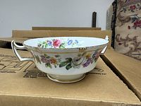 Large trifle bowl showing floral motif and scalloped gold rim placed on cardboard box