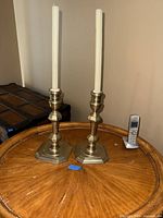Pair of brass candlesticks with white taper candles placed on wooden table.