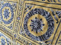 Close-up of wool needlepoint rug showing mustard yellow background and gray floral wreath motif