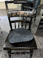 Front view of one black wooden chair showing hand-painted floral and fruit design on backrest, blue and white cushion on seat.