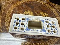Top view showing rectangular ceramic flower frog with multiple holes and blue decorative patterns.