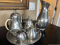 Full set of Royal Holland pewter including tea pot, sugar bowl, creamer, water pitcher, and tray displayed on a table with part of a mirror and wall switches in the background.