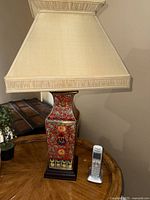 Full view of one red-base lamp with off-white shade and cordless phone for scale