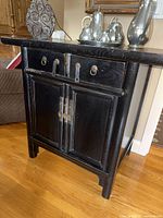 Full view of the black wooden side board, showing its shape, drawers, doors and metal details.