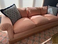 Long view of peachy-pink sofa with tassel fringe bottom and decorative pillows