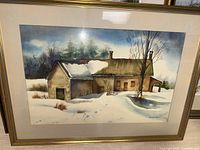 Framed watercolor winter scene depicting snowy rural buildings in gold-tone frame