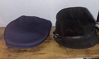 Navy blue and black hats displayed side by side on a wooden surface against a white wall background.