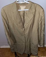 Front view of the tan Calvin Klein Sport blazer hanging on a white hanger showing three buttons, notch lapels, and front pockets.