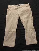White Capri pants laid flat showing front view, with belt loops and front pockets, cropped length with cuffed hem.