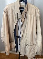 Front view of khaki lightweight jacket with drawstring at collar, button and snap closure, large front pockets and sleeve zipper pocket