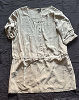 Light beige button-down dress with rolled sleeves and four pockets shown flat on fabric surface.