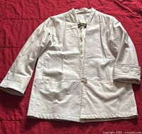 White leather jacket laid flat to show front side, with three-quarter sleeves and single button closure; collarless design with Daniel label inside collar.