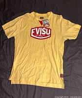 Front view of yellow Evisu T-shirt laid flat showing the red and white Evisu logo and original tags.