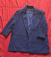 Front view of navy blue Forever 21 blazer size Medium laid flat on red background with sleeves slightly bent.