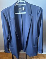 Front view of navy blue H&M blazer on hanger showing its notch lapel collar, long sleeves, two pockets, and smooth fabric texture.