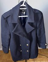 Front view of black H&M wool coat with double-breasted silver button closure, hanging on white hanger against plain background.