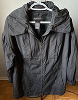 Front view of black windbreaker jacket on a hanger showing full length and collar details.