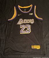 Front view of the black Lakers jersey with purple and yellow trim. Shows large Lakers logo and number 23.