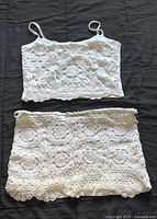 Front view of white lace halter top and matching mini skirt laid flat on dark surface
