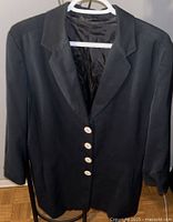 Front view of navy blue blazer jacket hanging on a white plastic hanger against a wall and wooden floor background.