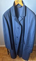 Front view of long navy blue trench coat hanging on wooden hanger, showing collar, button front closure, and long sleeves.