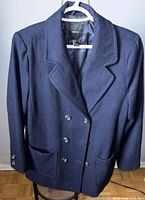 Front view of navy blue wool jacket on hanger showing double-breasted button closure and two front pockets.