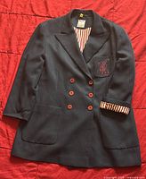 Navy blue blazer jacket laid flat showing front with red buttons and chest pocket monogram.
