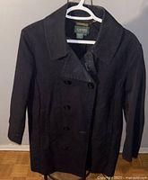 Front view of navy blue Ralph Lauren Lauren jacket on hanger against grey wall and wooden floor.