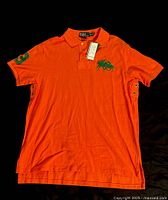 Front view of orange Ralph Lauren polo shirt size XL, showing embroidered green polo player logo on left chest and tags attached.