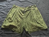 Pair of green pleated Ralph Lauren shorts with button details, front zipper, and cuffed hems on a dark fabric surface