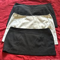 Lot of three Ralph Lauren mini skirts laid on red background. Two black skirts and one white skirt stacked.